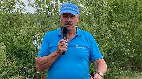 Ein Mann mit einem blauen T-Shirt und einer blauen Baseballkappe spricht in ein Mikrofon.