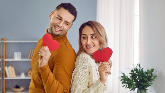 Ein Mann und eine Frau Rücken an Rücken mit roten Herzen in der Hand
