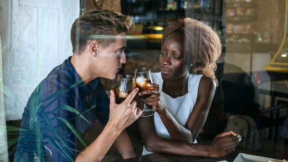 Ein junger Mann und eine junge Frau stoßen mit ihren Gläsern in einer Bar an