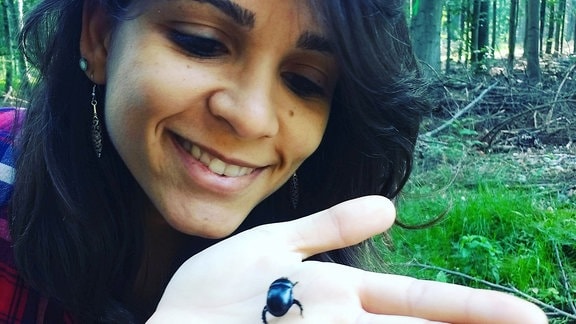 Eine Frau mit einem schwarzblauen Käfer auf der Hand