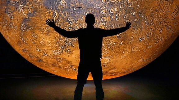 Silhouette eines Mannes mit ausgebreiteten Armen vor einem riesigen roten Marsmodell