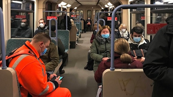Menschen sitzen in Zeiten der Coronapandemie mit medizinischen Mundmasken in einer vollen S-Bahn