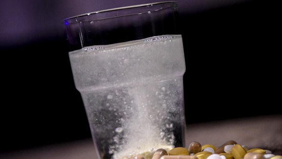 Ein Glas sprudelndes Wasser, davor liegen Medikamente 