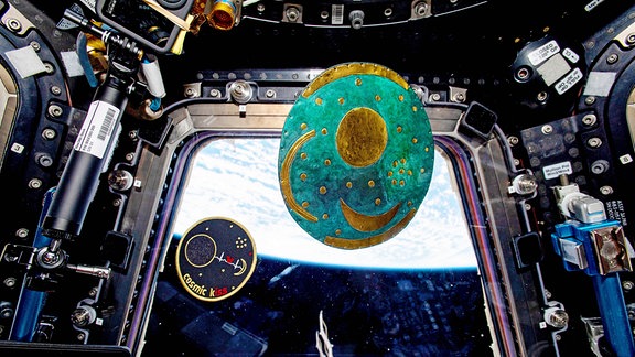 Eine Kopie der Himmelsscheibe von Nebra schwebt auf der Internationalen Raumstation ISS. Sie befindet sich in der Cupola, dem Weltraumfenster, von dem aus man die Erde im Hintergrund erkennen kann. Der deutsche Esa-Astronaut Matthias Maurer hatte sie mit auf die Raumstation genommen.