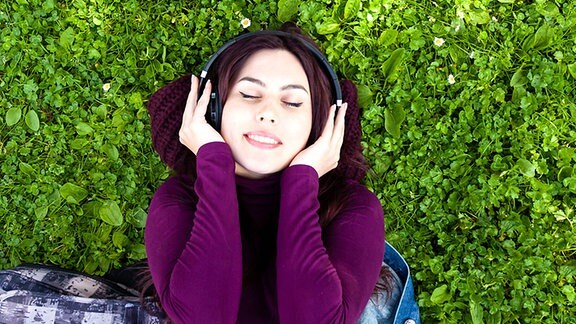 Eine junge Frau liegt mit Kopfhörern auf einer Wiese