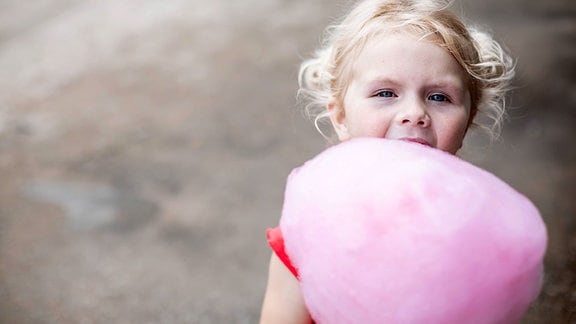 Ein Mädchen mit rosa Zuckerwatte in der Hand.