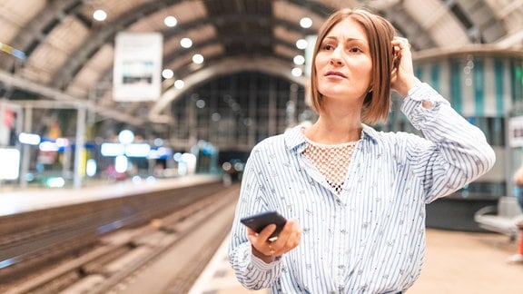 Eine junge Frau, die am Bahnhof ihr Smartphone benutzt.