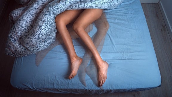Durch eine Langzeitbelichtung sieht man Beine in einem Bett an verschiedenen Positionen.