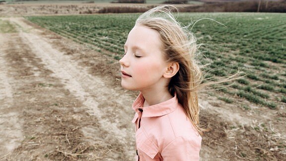 Mädchen mit geschlossenen Augen vor einem Feldweg