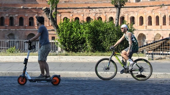 Ein E-Scooterfahrer und ein Radfahrer auf einer Straße.