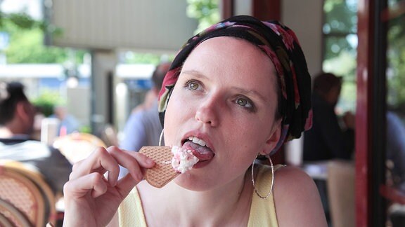 Eine junge Frau mit Kopftuch sitzt allein in einem Cafe und isst einen Eisbecher