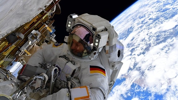 Der deutsche Esa-Astronaut Matthias Maurer befindet sich auf einem Außeneinsatz auf der ISS. Im Hintergrund kann man die blaue Erde und das schwarze Weltall sehen.