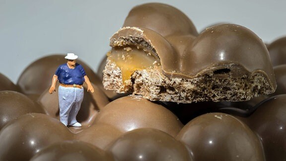 Symbolbild Übergewicht durch Süßigkeiten - Figur eines Dicken Mannes steht auf Schokolade.