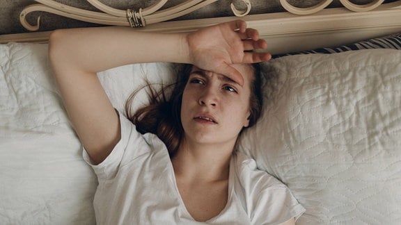 Eine junge Frau mit Kopfschmerzen liegt zu Hause im Bett.