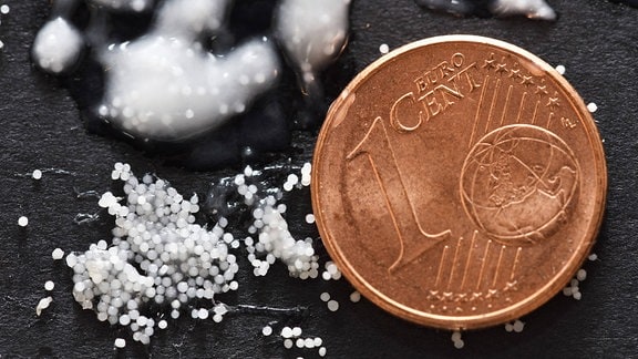 Mikroplastik-Partikel im Größenvergleich neben einer Ein-Cent-Münze