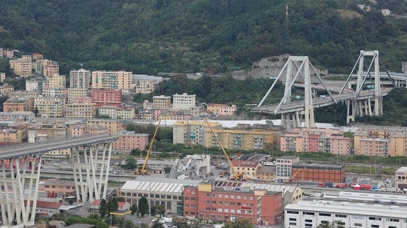 Teileingestürzte Brücke mit Tragseilen über bebautem Tal und Hang