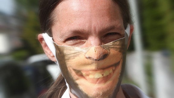 Eine Person trägt eine Mund- und Nasenschutzmaske mit Aufdruck eines lachenden Schimpansen.