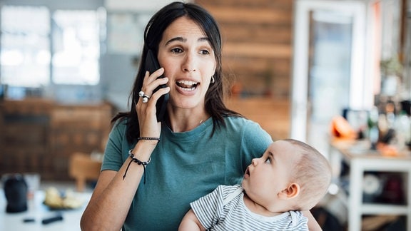 Eine Frau telefoniert während sie ein Baby auf dem Arm hat.