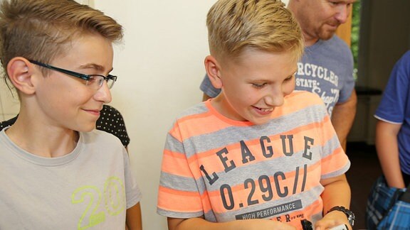 Ein Junge mit einem Lego-Liga-T-Shirt drückt Tasten an dem Lego-Roboter.