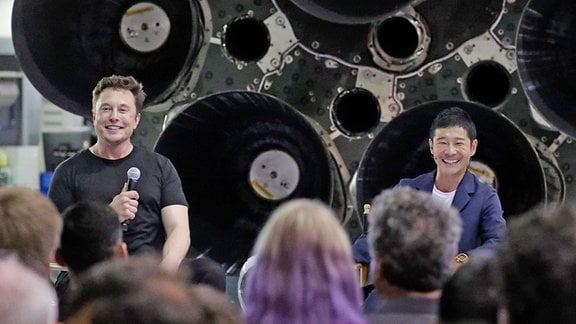 Elon Musk und Yusaku Maezaw präsentieren das DearMoon-Projekt vor den Raketentriebwerken des Starships.