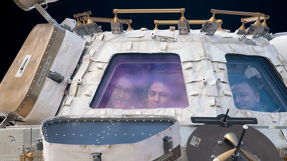 Zwei Astronautinnen und ein Astronaut schauen aus der Beobachtungskuppel der ISS
