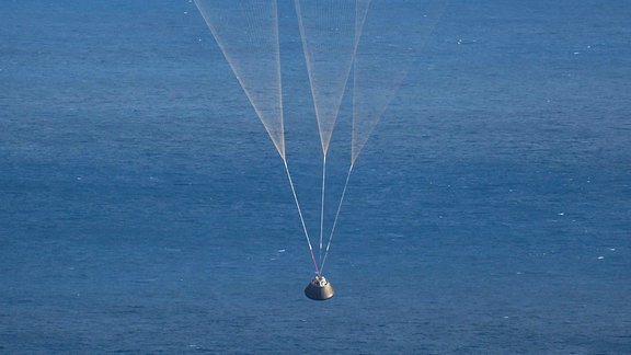 Raumkapsel mit Fallschirm am Himmel