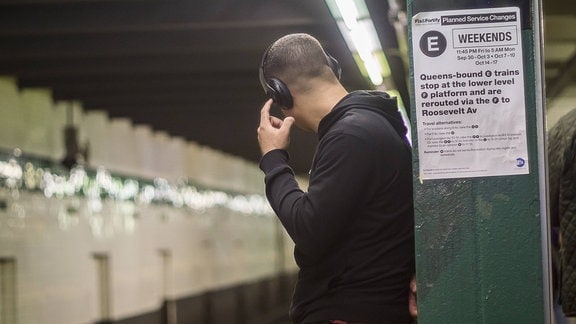 Mann mit Kopfhörern in einer U-Bahn-Station mit dem Rücken zum Betrachter, drückt auf einen Knopf am Kopfhörer