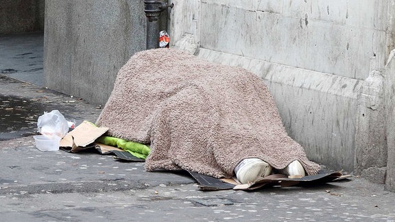 Ein Obdachloser liegt zugedeckt auf einem Fußweg.