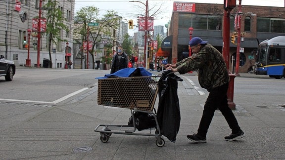 Ein Obdachloser schiebt einen Einkaufswagen mit Habseligkeiten