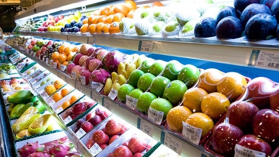 Supermarkt-Auslage mit Obst in vielen Farben, vor allem Äpfel und Zitrusfrüchte. Viele im Viererpark in Folie eingescheist. Perspektive mit Unschärfe nach schräg hinten.
