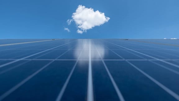 Eine Wolke spiegelt sich in einer Photovoltaik-Freiflächenanlage auf einem Solarpark. 