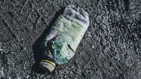 eine alte, kaputte Saftflasche aus Plastik auf einer Schotterstrasse