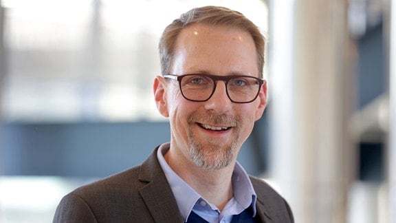 Das Bild zeigt einen lächelnden Mann mit kurzen Haaren und Brille im Anzug, den Chronobiologen Thomas Kantermann