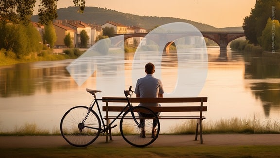 Ein Mann blickt von einer Bank am Ufer auf eine Flusslandschaft. An der Bank lehnt sein Fahrrad.