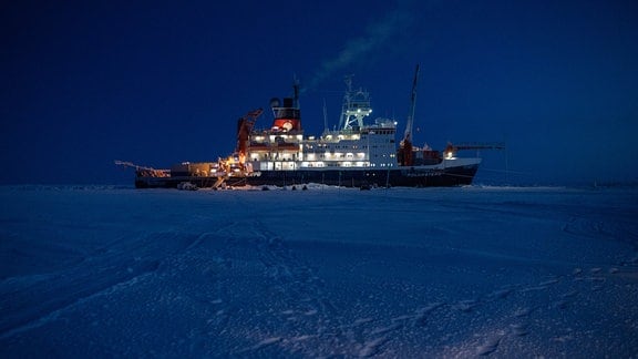 Ein Forschungsschiff in Dämmerung, fast dunkel, Schiff betriebsam leuchtend, umgeben von Eis