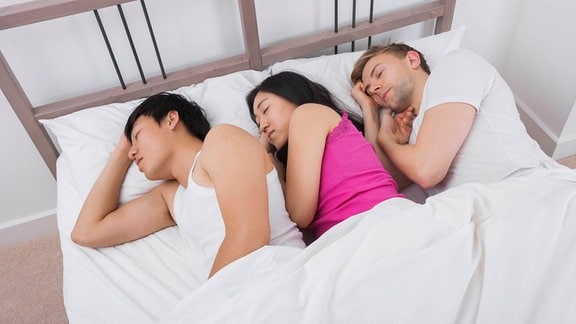 Eine Frau und zwei Männer liegen zusammen im Bett