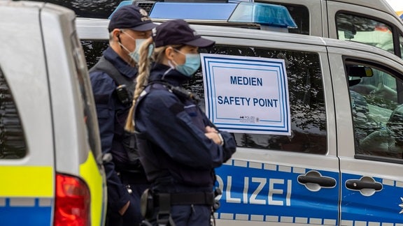 Medien Safety Point steht auf Schildern an Polizeiwagen, neben denen Polizisten stehen.
