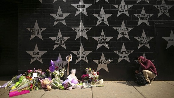 Trauernder Prince -Fan vor einer Mauer mit Sternen und Blumengebinden.