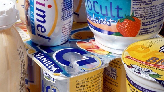 Verschiedene Joghurt-Drinks in kleinen Plastikfläschchen und Joghurtbecher mit bunten Etiketten, alle mit angeblich probiotischer Funktion, stehen übereinander gestapelt.