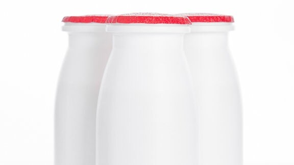 Drei weiße Plastikfläschchen mit für Probiotik-Drinks typischer Erscheinung und abziehbarem Alu-Deckel.