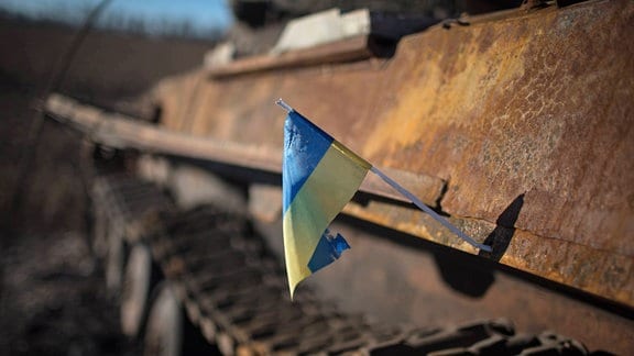 Eine ukrainische Flagge hängt an einem ausgebrannten Panzer