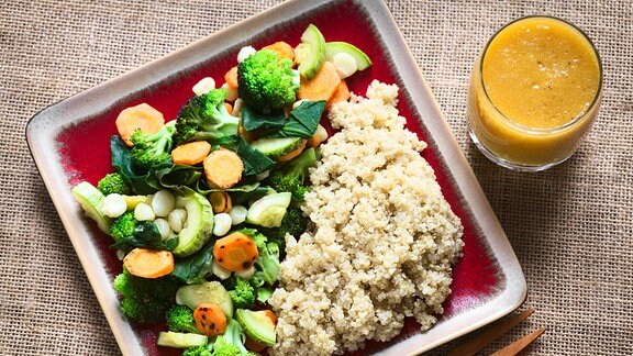 Gemüse und Quinoa auf einem Teller neben einem Glas mit Saft