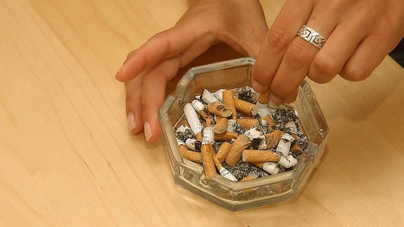 Junge Raucherin drückt ihre Zigarette in einem vollen Aschenbecher aus.