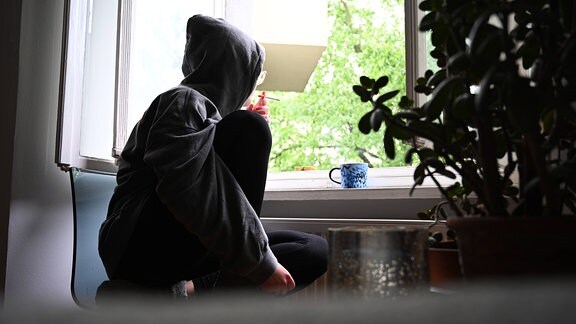 Einsamkeit- eine junge Frau schaut rauchend aus dem Fenster
