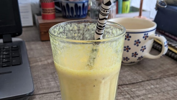 Ein Glas mit einem Bananen-Kurkuma-Smoothie und Strohhalm.