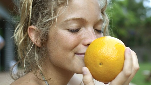 Eine junge Frau riecht an einer Orange