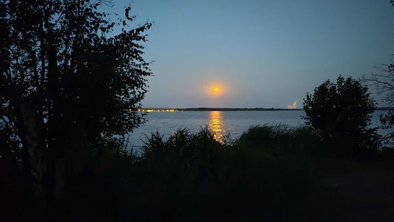 Ein rot schimmernder Vollmond über dem Cospudener See in Leipzig.