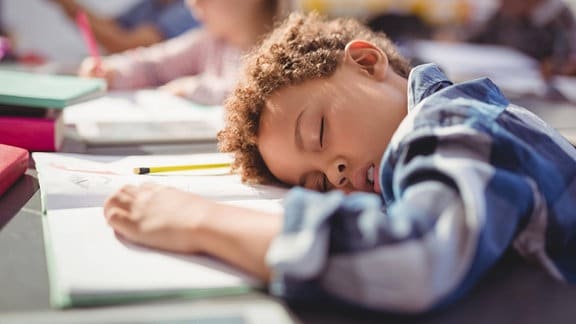 Ein Müder Schüler schläft mit dem Kopf auf der Schulbank.