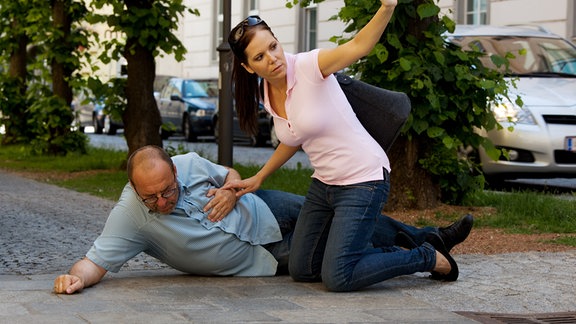 Ein Mann liegt mit Schmerzen auf der Straße und eine Frau hilft ihm