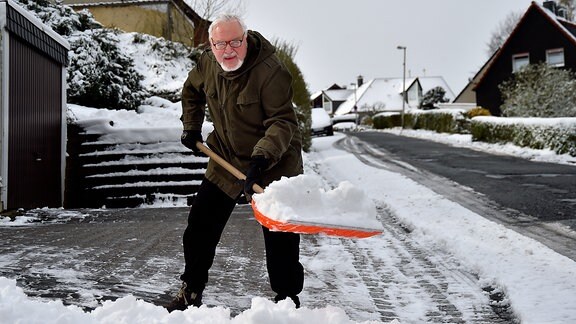 Ein Mann räumt den Gehtweg von Schnee frei.